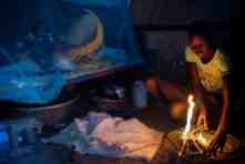 A girl builds a fire to make tea while her mother cares for a baby under a mosquito net in their shelter. According to UN figures, an adolescent girl in South Sudan is three times more likely to die in childbirth than to have completed her primary education